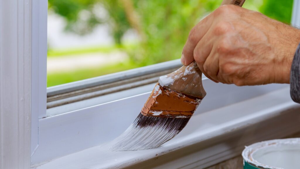 Painting a wooden window paint with paintbrush while painting window trim